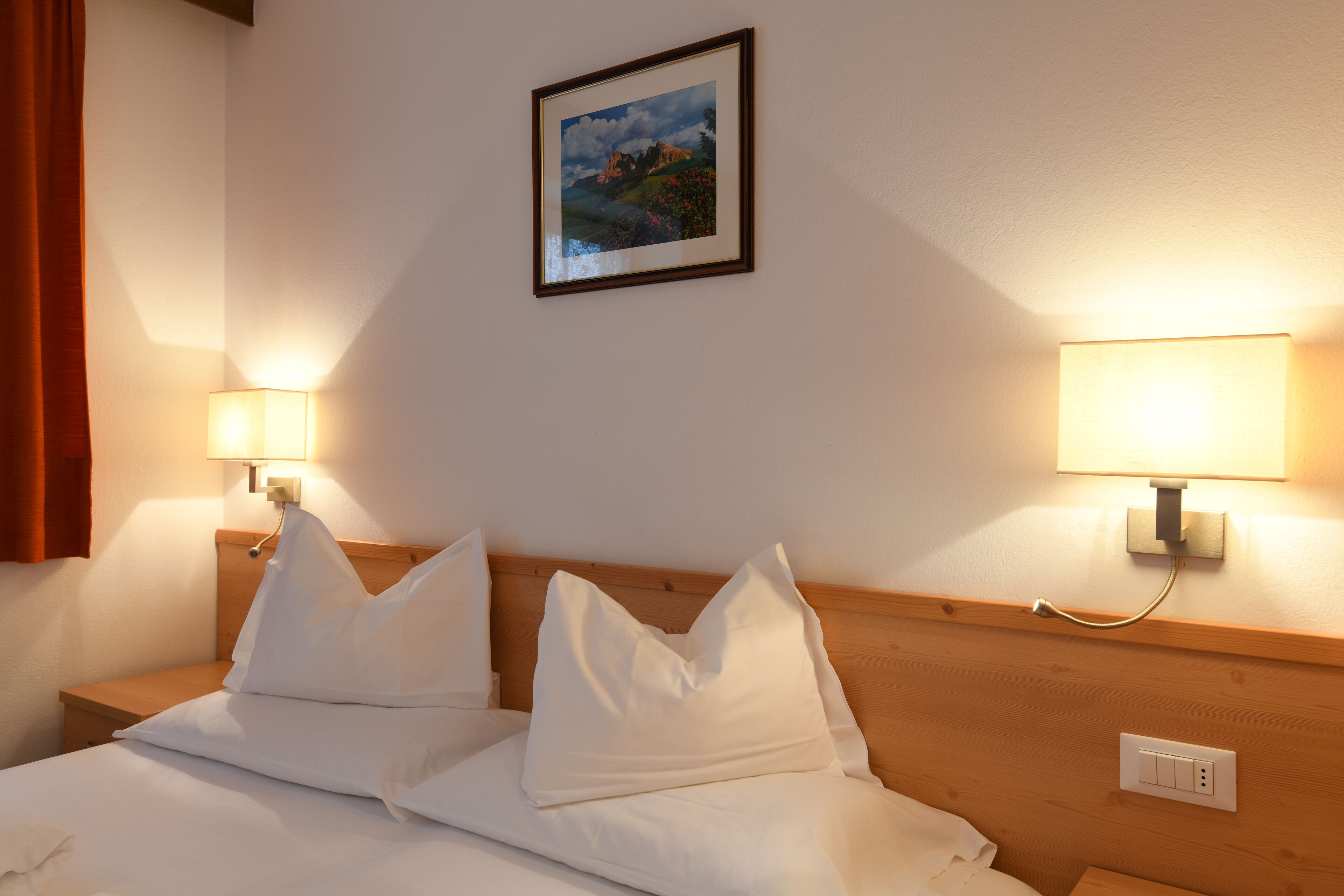Camera d'albergo con un letto rifatto, due lampade ai comodini, un quadro appeso alla parete e una testiera in legno.