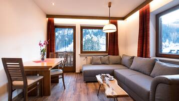 Uma sala de estar aconchegante com uma mesa de jantar de madeira, um sofá e vista para uma paisagem montanhosa coberta de neve através de grandes janelas.