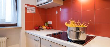 Una cocina con estufa, una olla de espagueti y un microondas encima.