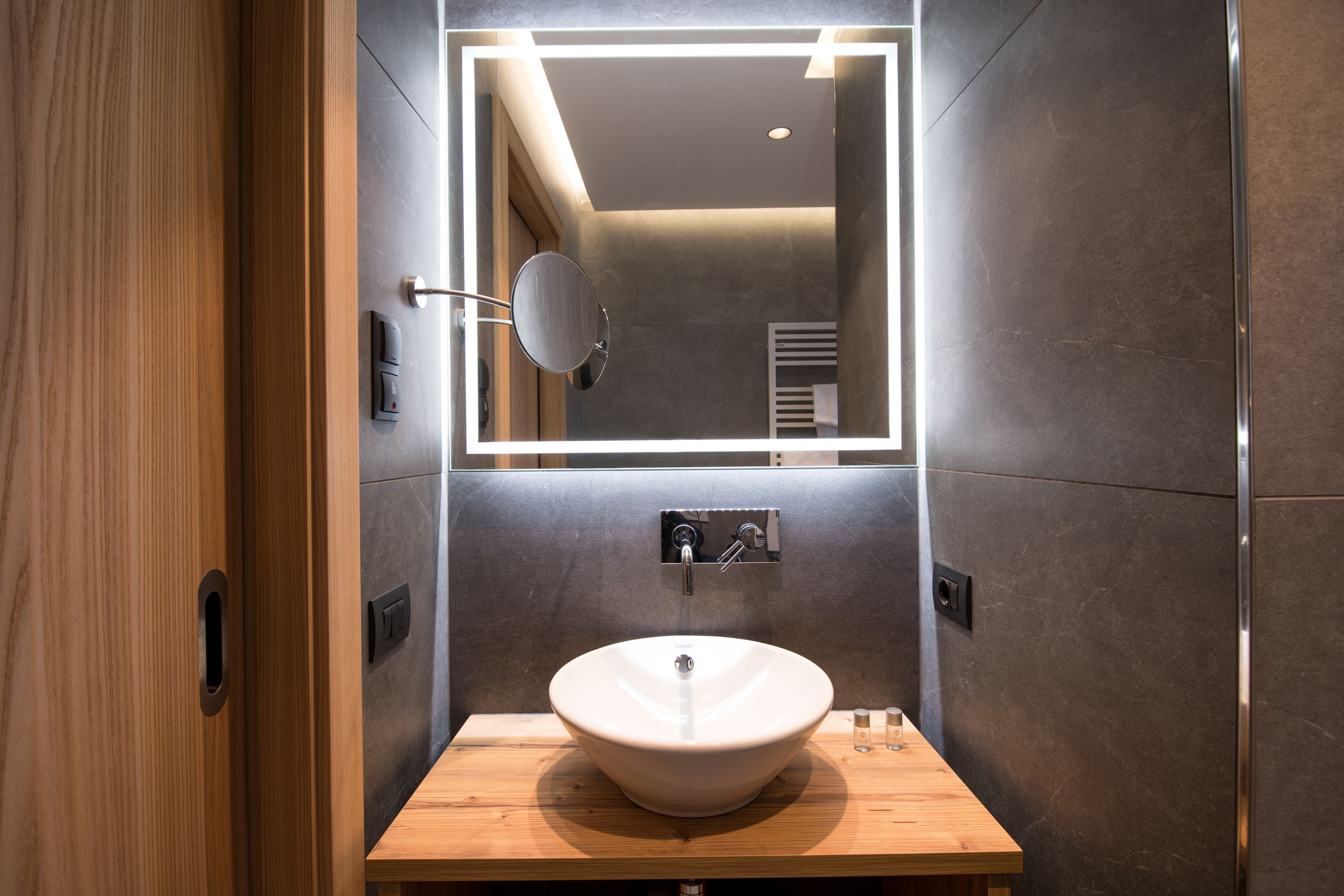 Un baño moderno con tocador de madera, espejo redondo y lavamanos integrado.