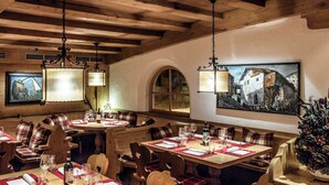 Un restaurante con vigas de madera, mesas redondas y bancos. Hay lámparas colgantes y un cuadro en la pared.