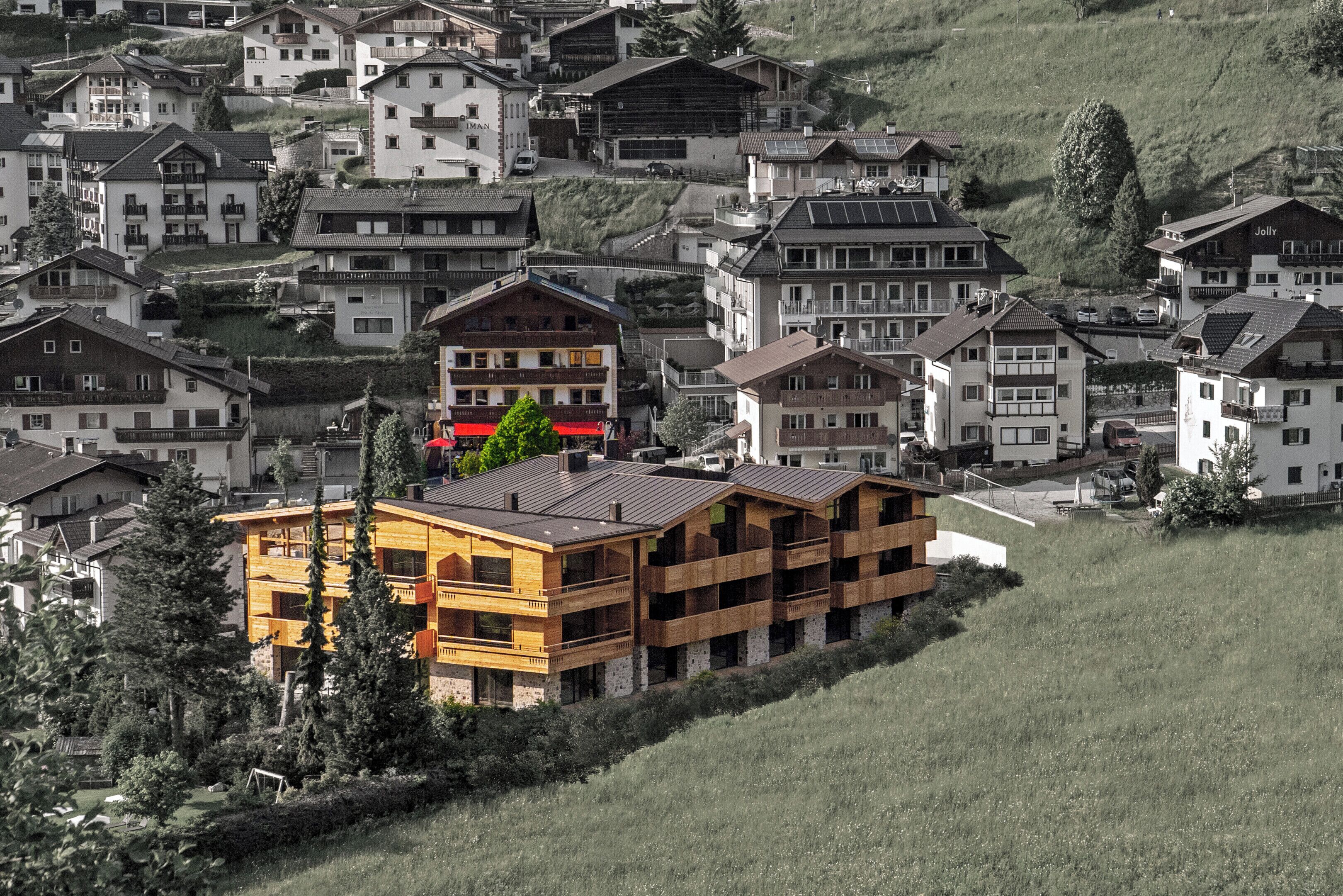 Un edificio moderno de varios pisos con balcones, rodeado de casas tradicionales en una ladera.