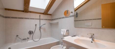 Ein modernes Badezimmer mit Dachfenster, einer Badewanne, einem Bidet, einem Waschbecken und einem Spiegel.