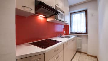 A kitchen with red tiles, a built-in microwave, a stove, and a window with curtains.