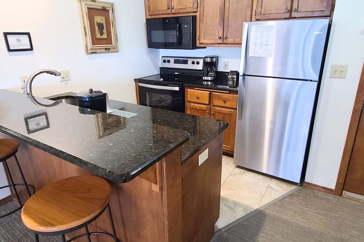 A kitchen with wooden cabinets, a stainless steel refrigerator, a microwave, an oven, and a coffee maker.