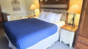 A neatly made bed with a blue blanket, two bedside tables with lamps, a wooden headboard, and a decorative wall piece.