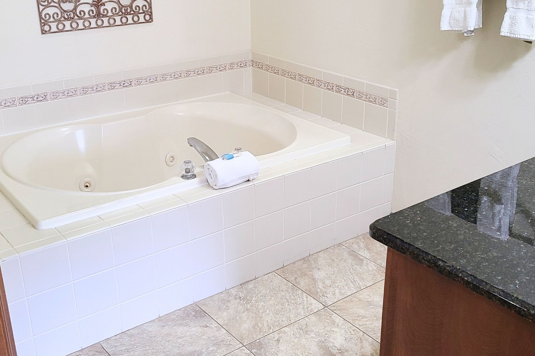 A bathroom with a bathtub, white tiles, a decorative wall piece, and a black countertop.