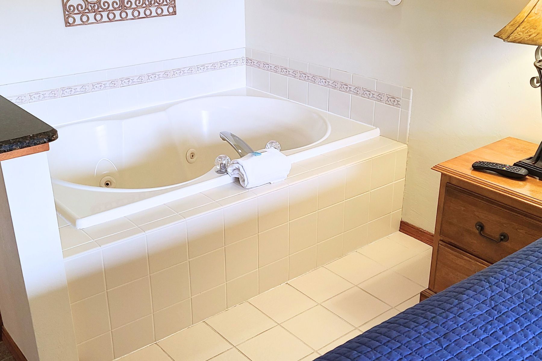 A bathroom with a bathtub, a wooden nightstand with a remote control, and a blue bed.