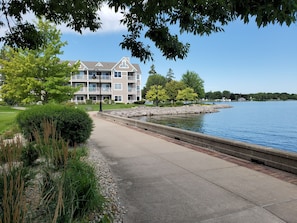 A waterfront property with a paved walkway, a stone retaining wall, and a large building with multiple balconies. - Bridgeport Waterfront Resort (Sturgeon Bay)