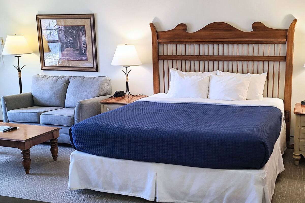 A hotel room with a large bed, a sofa, two bedside tables, and a framed picture on the wall.