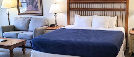 Una camera d'albergo con un letto grande, un divano, due comodini e un quadro appeso al muro.