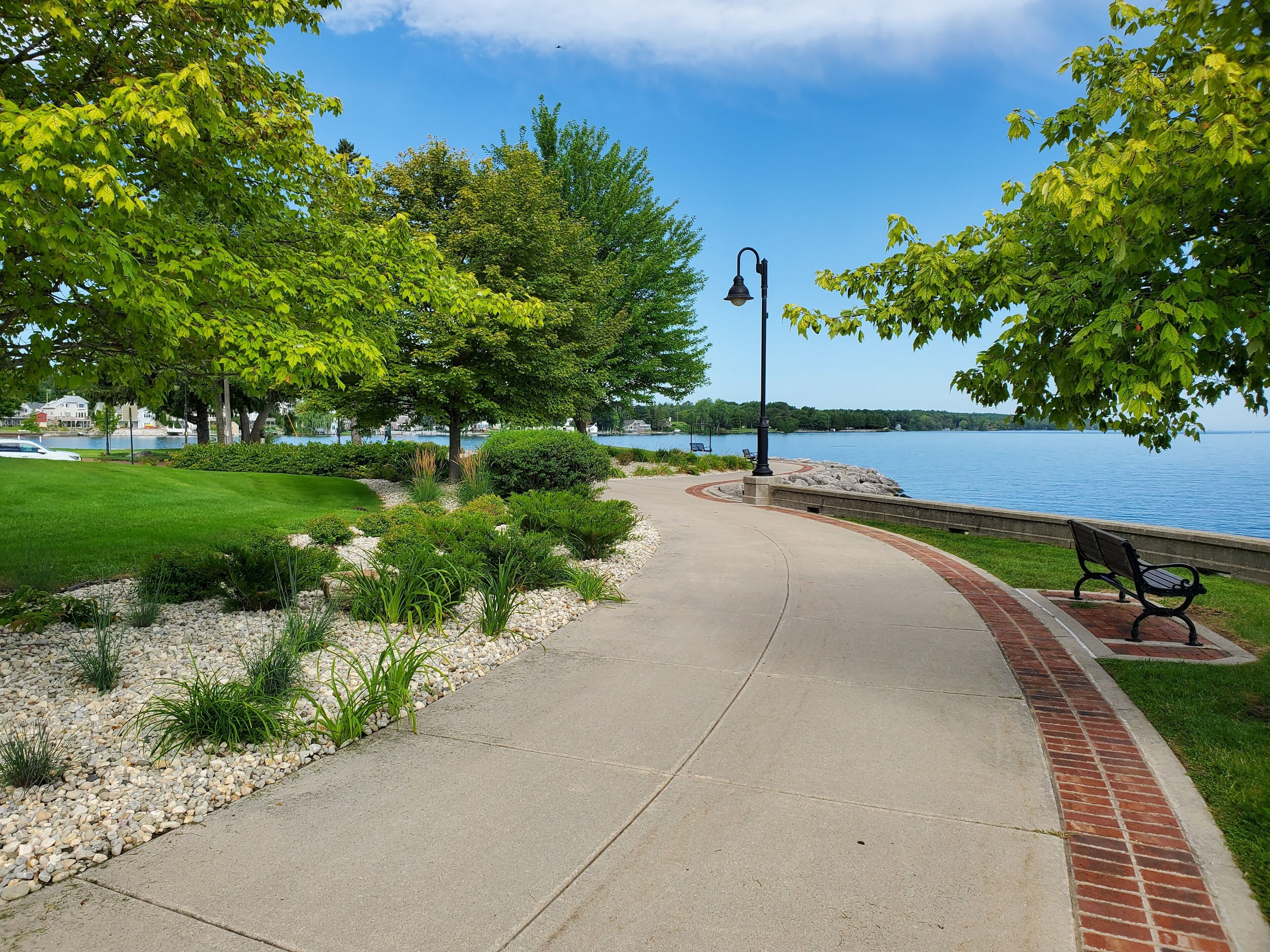 Un sentier dans un parc, avec un banc, un lampadaire et une vue sur un lac.