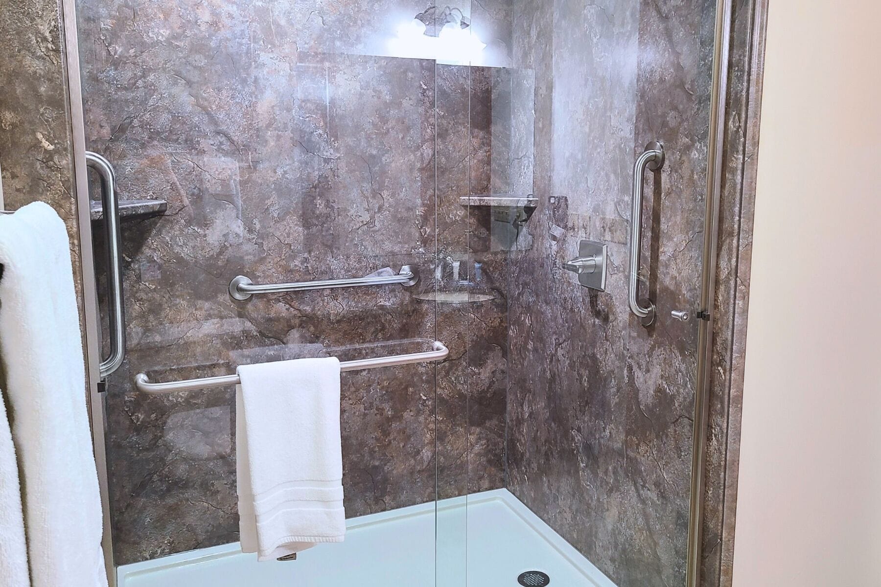 A bathroom with a shower, grab bars, and a towel rack.