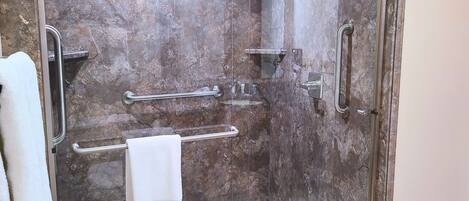 A bathroom with a shower, grab bars, and a towel rack.