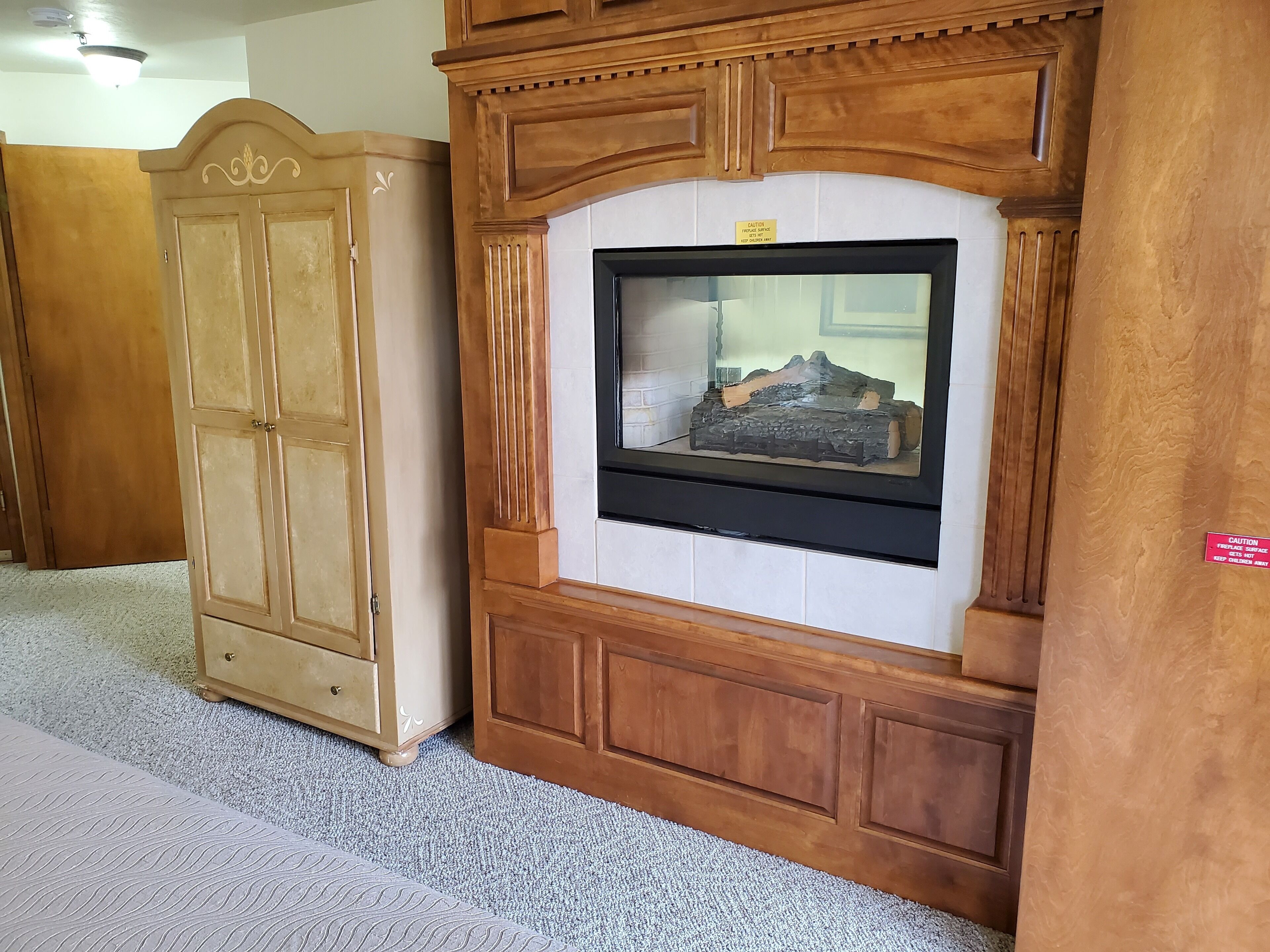 Une pièce avec un meuble en bois, un téléviseur fixé au mur, également en bois, et un sol recouvert d’une moquette.