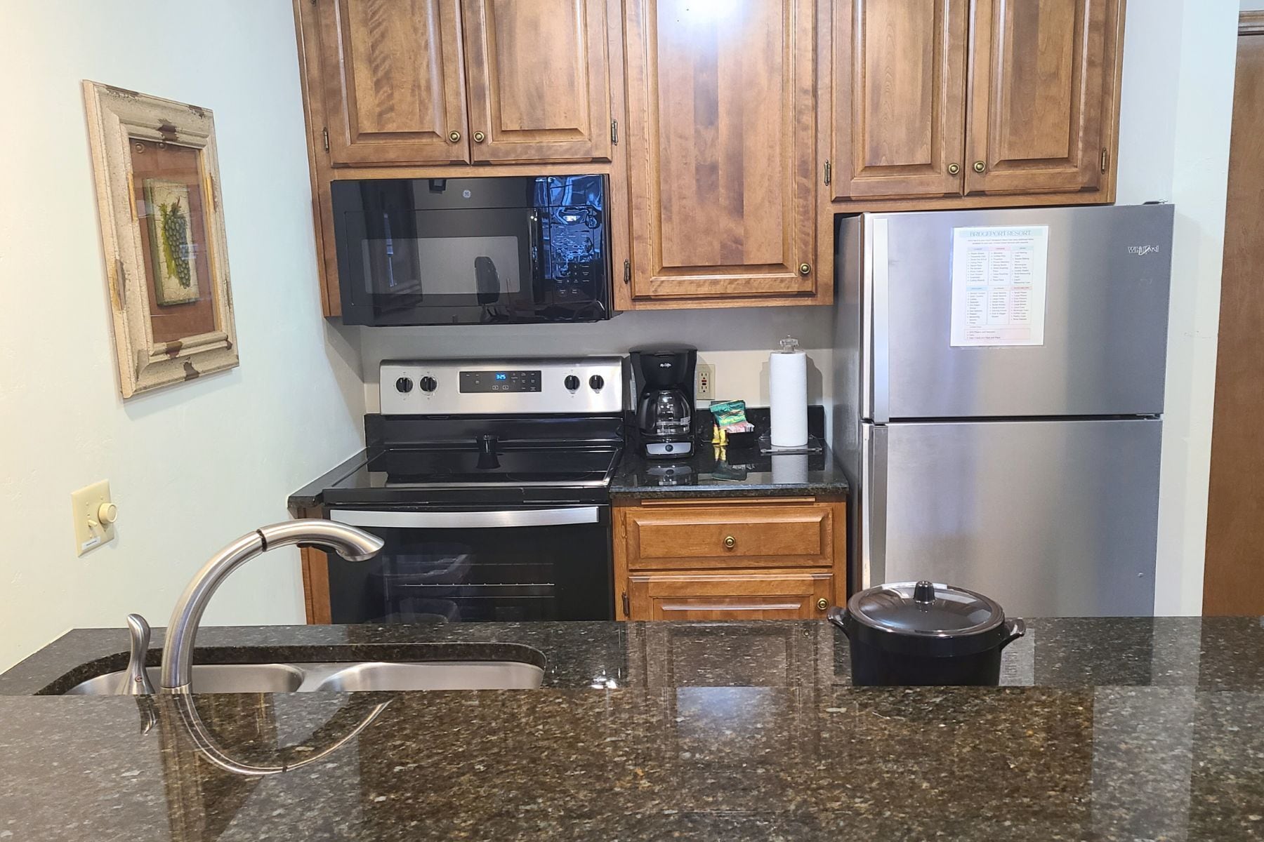 A kitchen with wooden cabinets, a stainless steel refrigerator, a microwave, an oven, a sink, and a granite countertop.