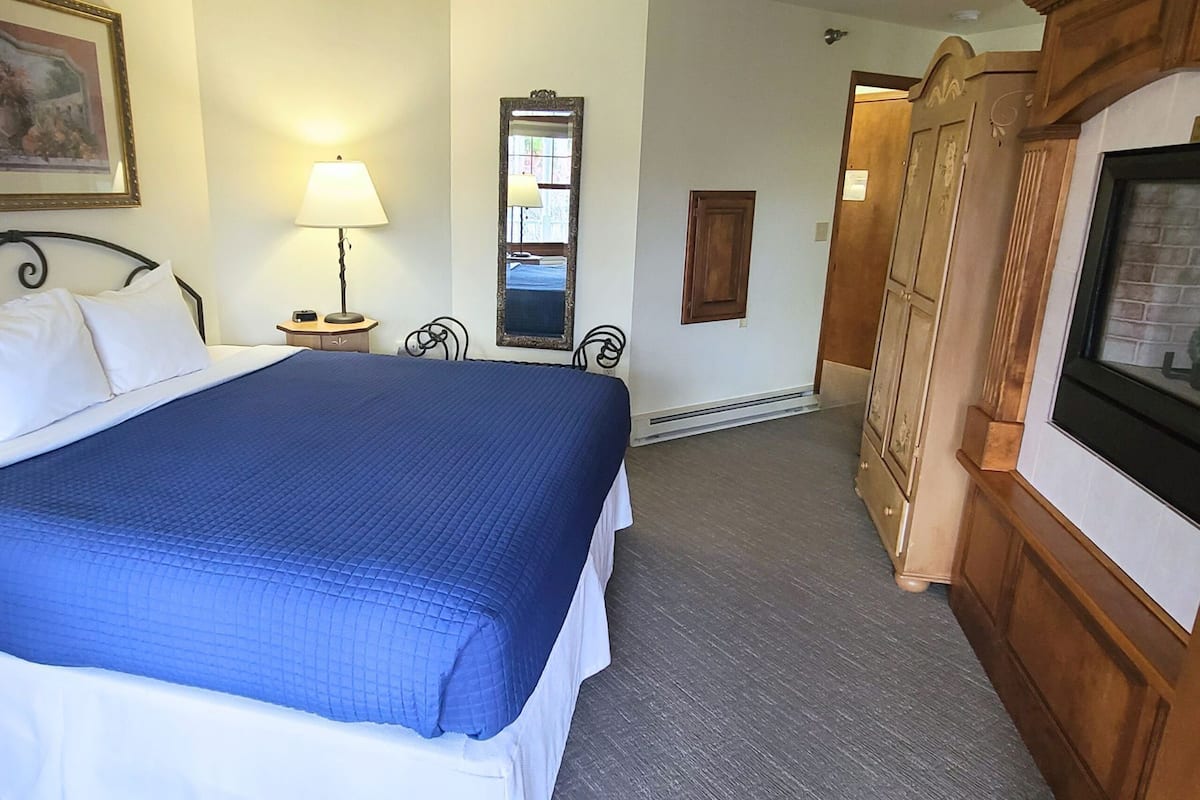 A hotel room with a large bed, a bedside lamp, a mirror, a wooden wardrobe, and a television.