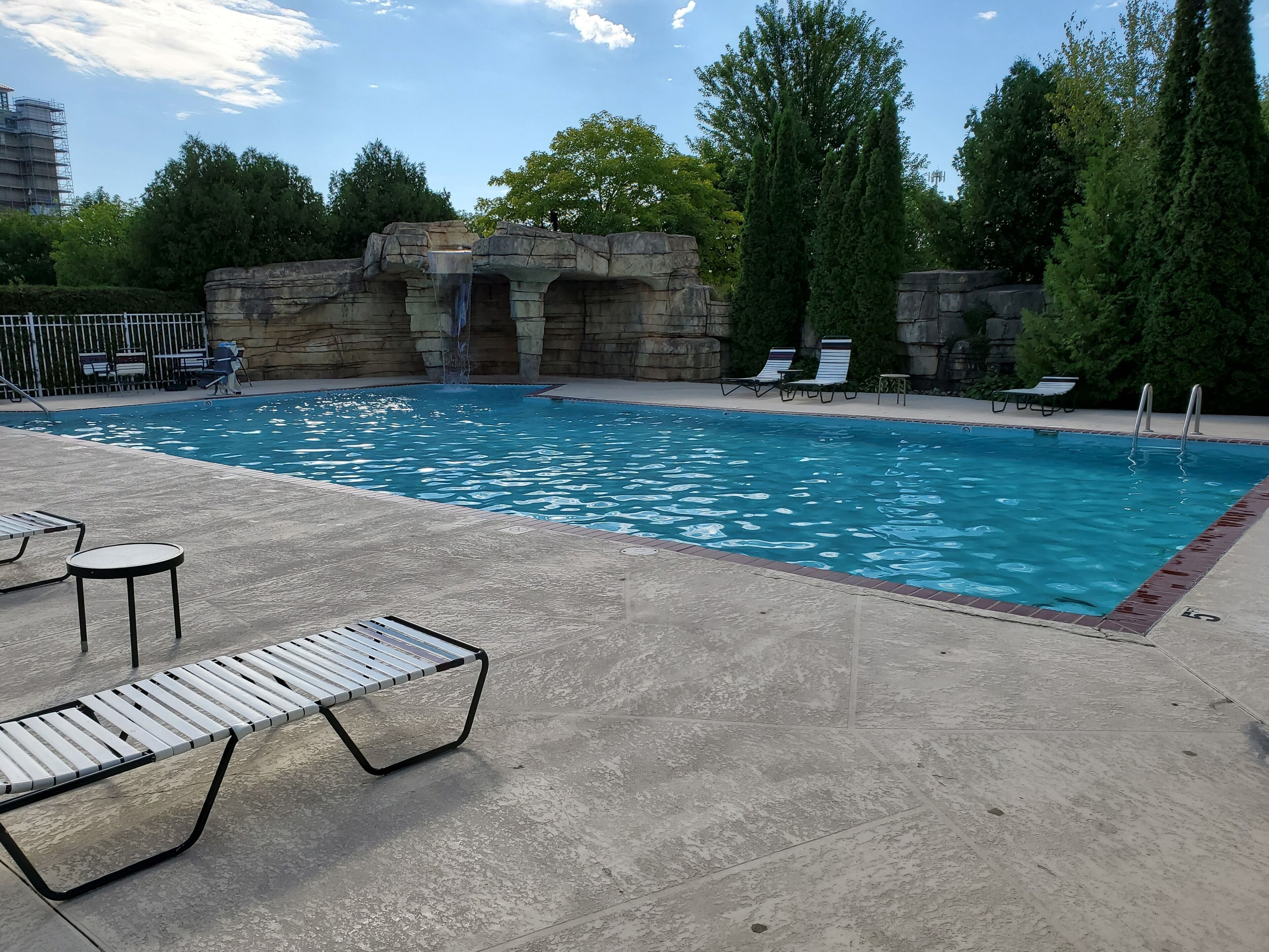 A swimming pool with a waterfall feature, surrounded by lounge chairs and a stone wall.