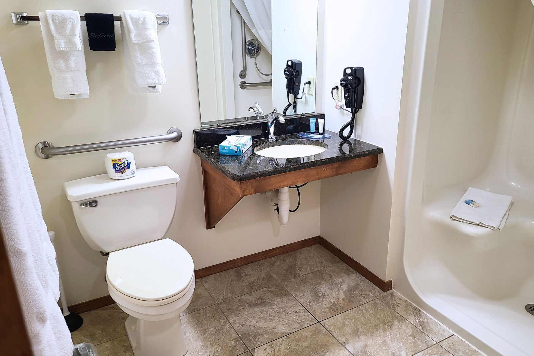 A bathroom with a toilet, sink, and shower. There is a hand dryer and a hairdryer on the wall.