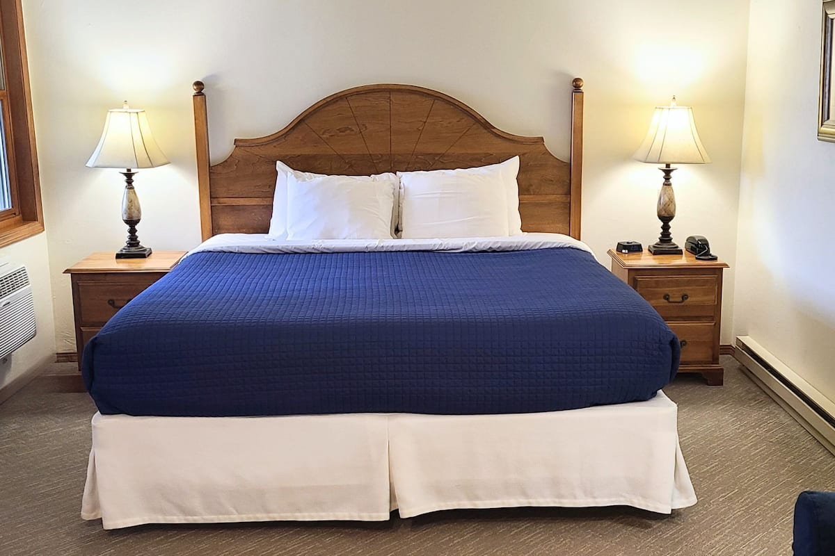 A neatly made bed with a wooden headboard, two bedside tables with lamps, and a white wall.