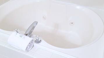 A white bathtub with a silver faucet and two holes, a rolled white towel, and a white tiled wall with a decorative border.