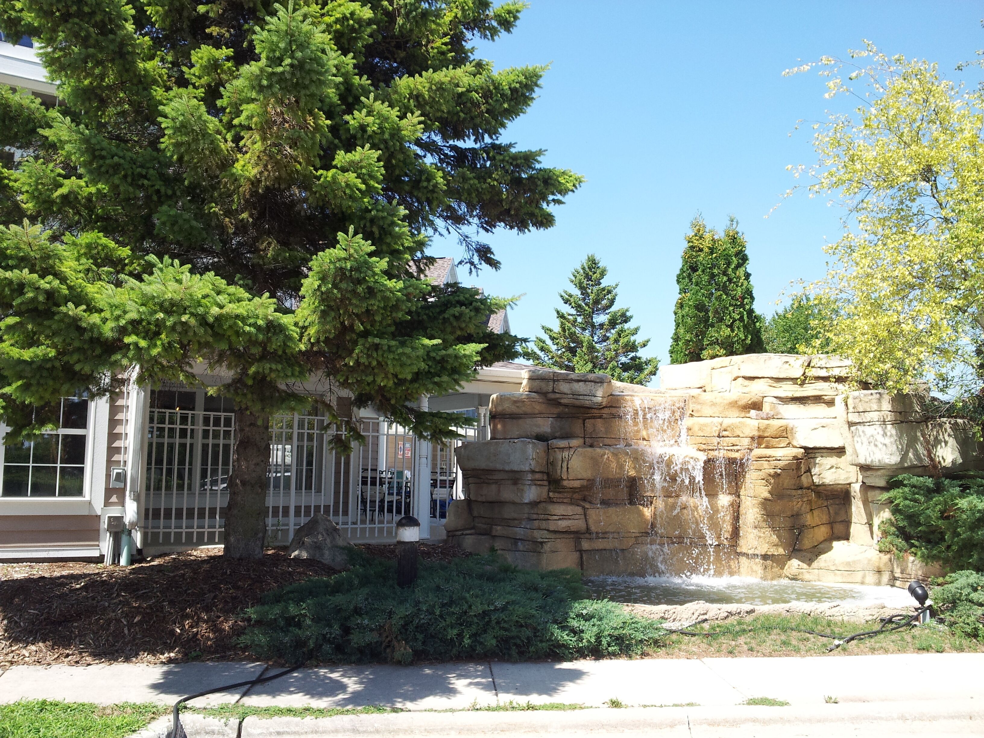 A building with a waterfall feature, surrounded by trees and a stone wall.