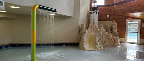 A water feature with a waterfall and a mountain-like structure in a spacious indoor area with wooden walls and a tiled floor.
