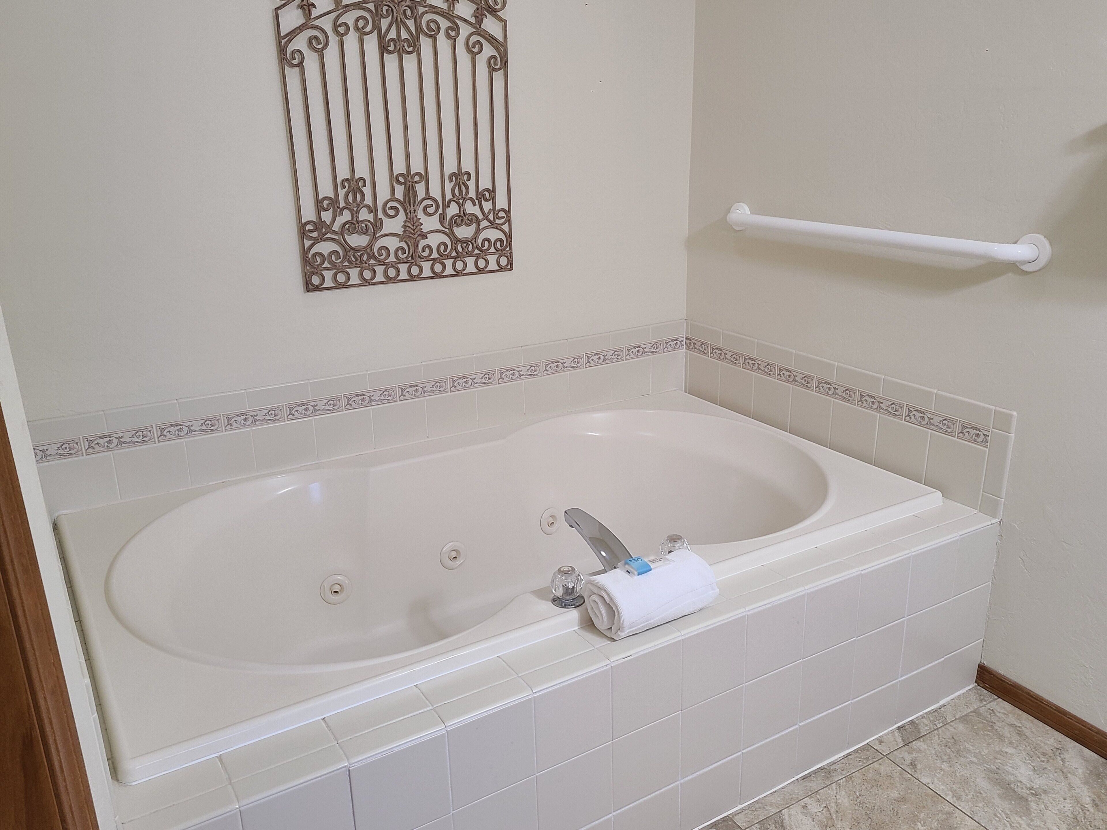 A bathroom with a large bathtub, a towel rack, and decorative wall tiles.
