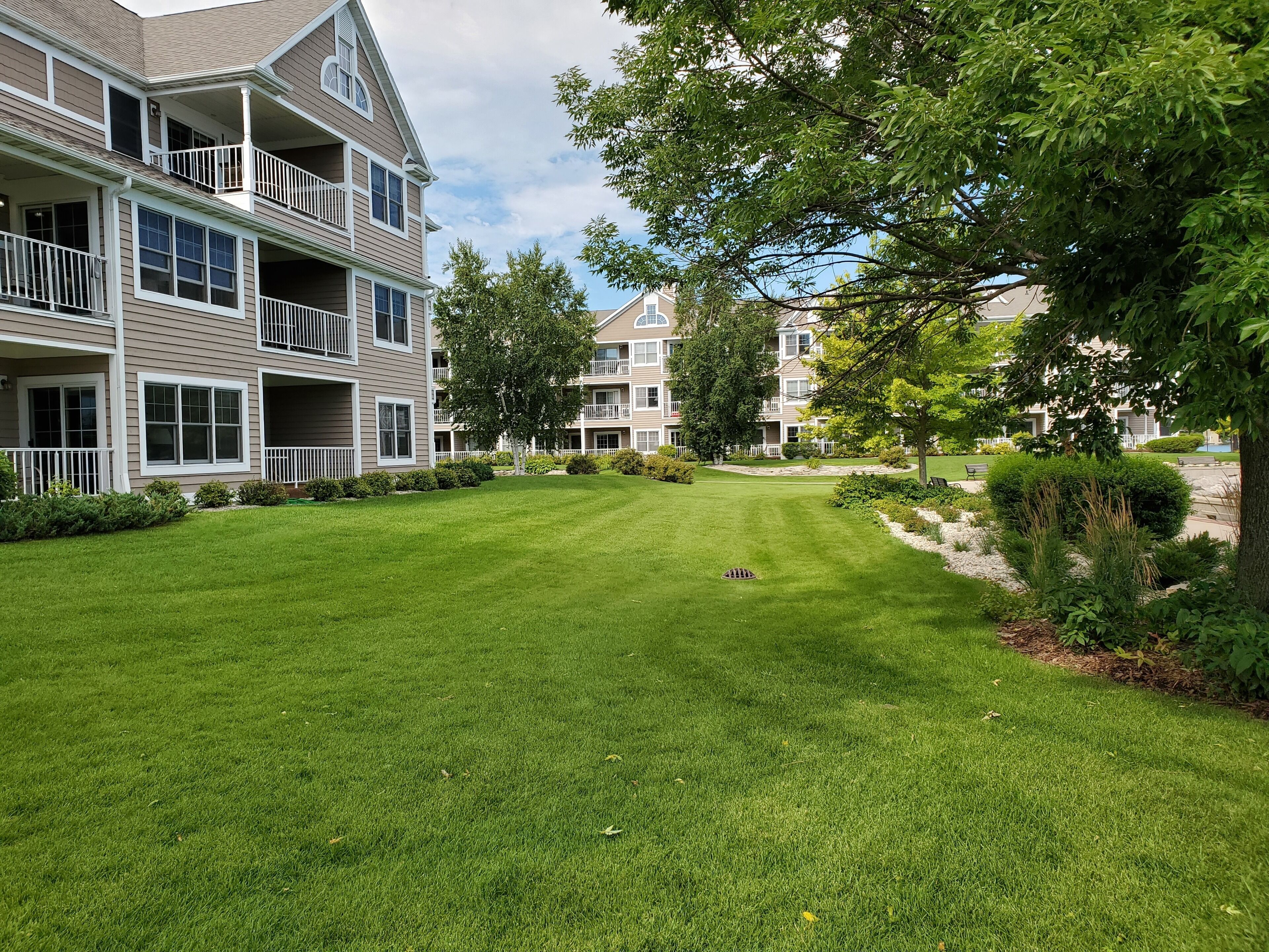 A multi-story residential building with a well-maintained lawn, trees, and a clear sky.
