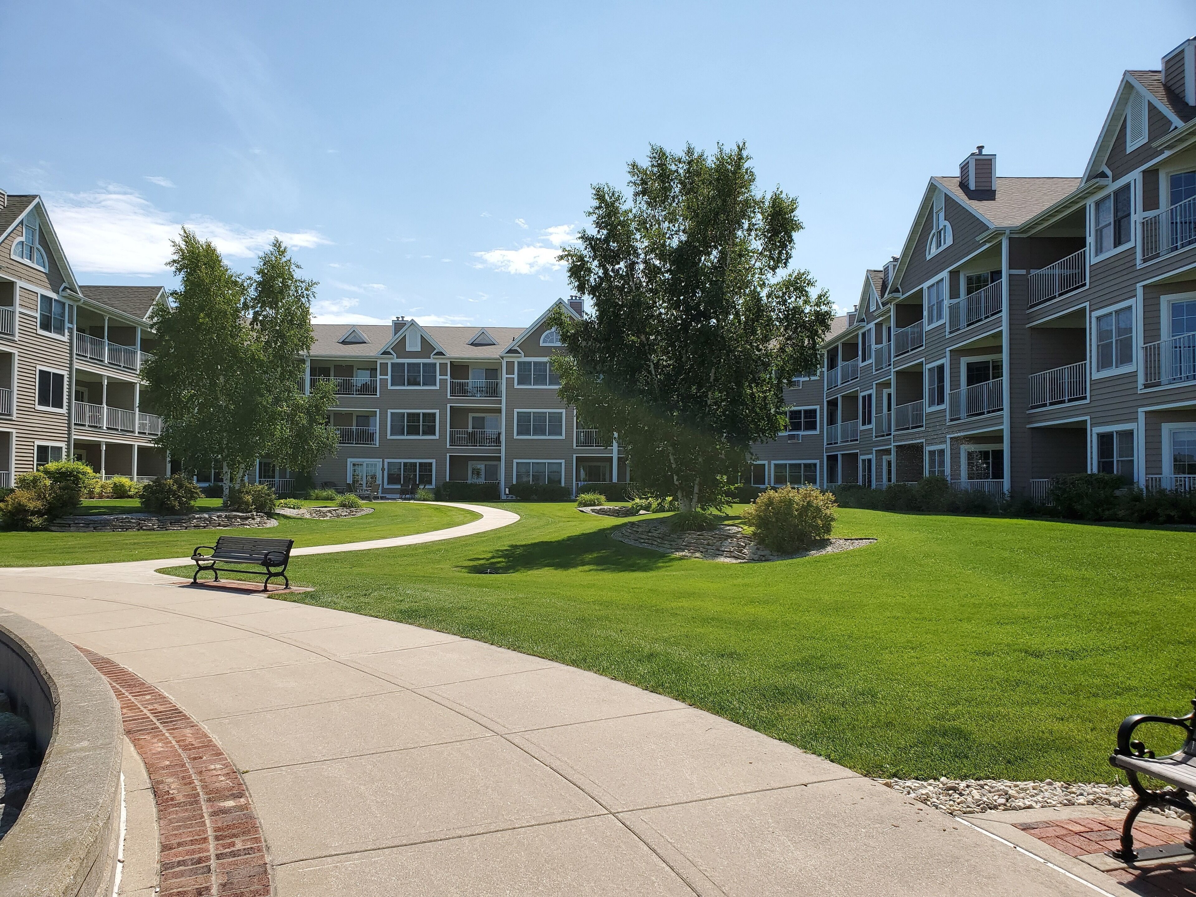 A residential building with multiple balconies, a paved walkway, and a well-maintained lawn.