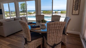 Comedor con sillas de mimbre y una mesa de vidrio, con vista a una piscina y una playa.