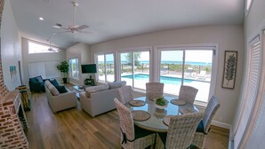Amplia sala de estar con vista a la piscina, mobiliario de mimbre y televisor de pantalla plana.
