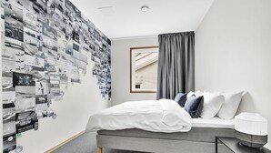 Una habitación de hotel moderna con una cama gris, ropa de cama blanca, una alfombra gris, una cortina gris y una pared decorada con fotografías en blanco y negro.