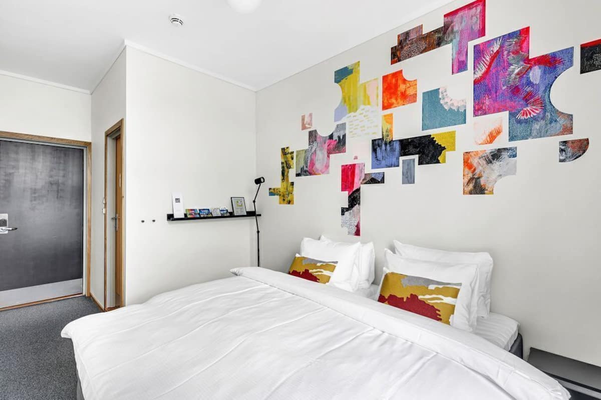 A modern hotel room with a large bed, a wall art installation, and a small shelf with items.