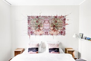 A bedroom with a large bed, two bedside tables, a nightstand, and a wall-mounted artwork. - Lille Hotell (Arendal)