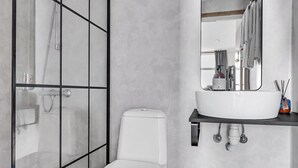Un baño moderno con cabina de ducha de vidrio, inodoro blanco y tocador con espejo y lavamanos.