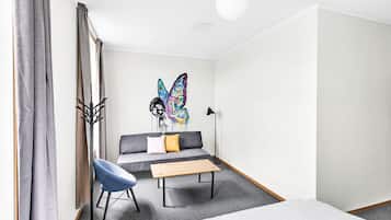 Een moderne hotelkamer met een grijze bank, een blauwe stoel, een houten salontafel en kleurrijke vlinderkunst aan de muur.