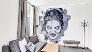 Una sala de estar moderna con un sofá gris, una mesita de madera, un banco gris y una gran obra de arte abstracta en la pared.