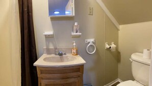 A bathroom with a wooden vanity, a sink, a toilet, and a shower area. - Sportsman Cottage - Raystown Lake Vacation Rentals, Aunt Susie's (Hesston)