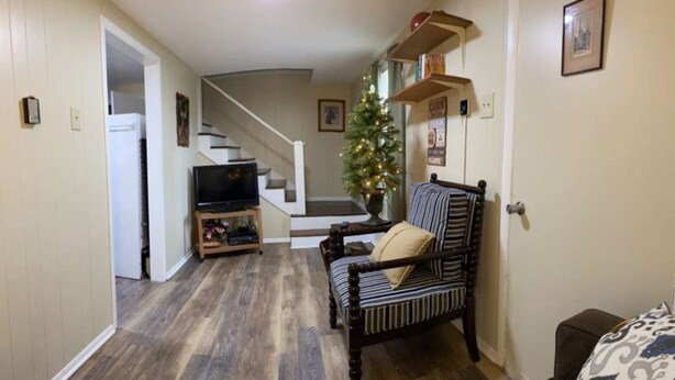 A living room with a wooden floor, a television on a stand, a striped sofa, and a staircase leading to another level. - Sportsman Cottage - Raystown Lake Vacation Rentals, Aunt Susie's (Hesston)