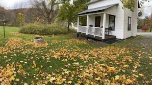 A small white house with a porch, surrounded by a lawn covered in fallen leaves. - Sportsman Cottage - Raystown Lake Vacation Rentals, Aunt Susie's (Hesston)