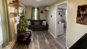 A cozy living room with a dark brown sofa, a small wooden coffee table, and a lit Christmas tree. - Sportsman Cottage - Raystown Lake Vacation Rentals, Aunt Susie's (Hesston)