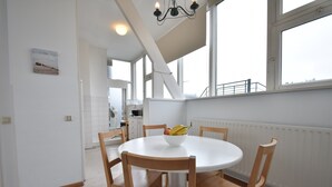 Una mesa redonda para comer con sillas de madera, un cuenco de fruta y vistas a un paisaje urbano a través de ventanas amplias.