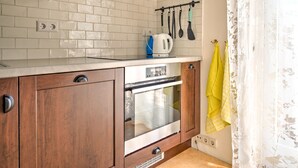 Une cuisine avec des carreaux de céramique blancs disposés en motif métro, des armoires en bois, un four encastré et une bouilloire posée sur le plan de travail.