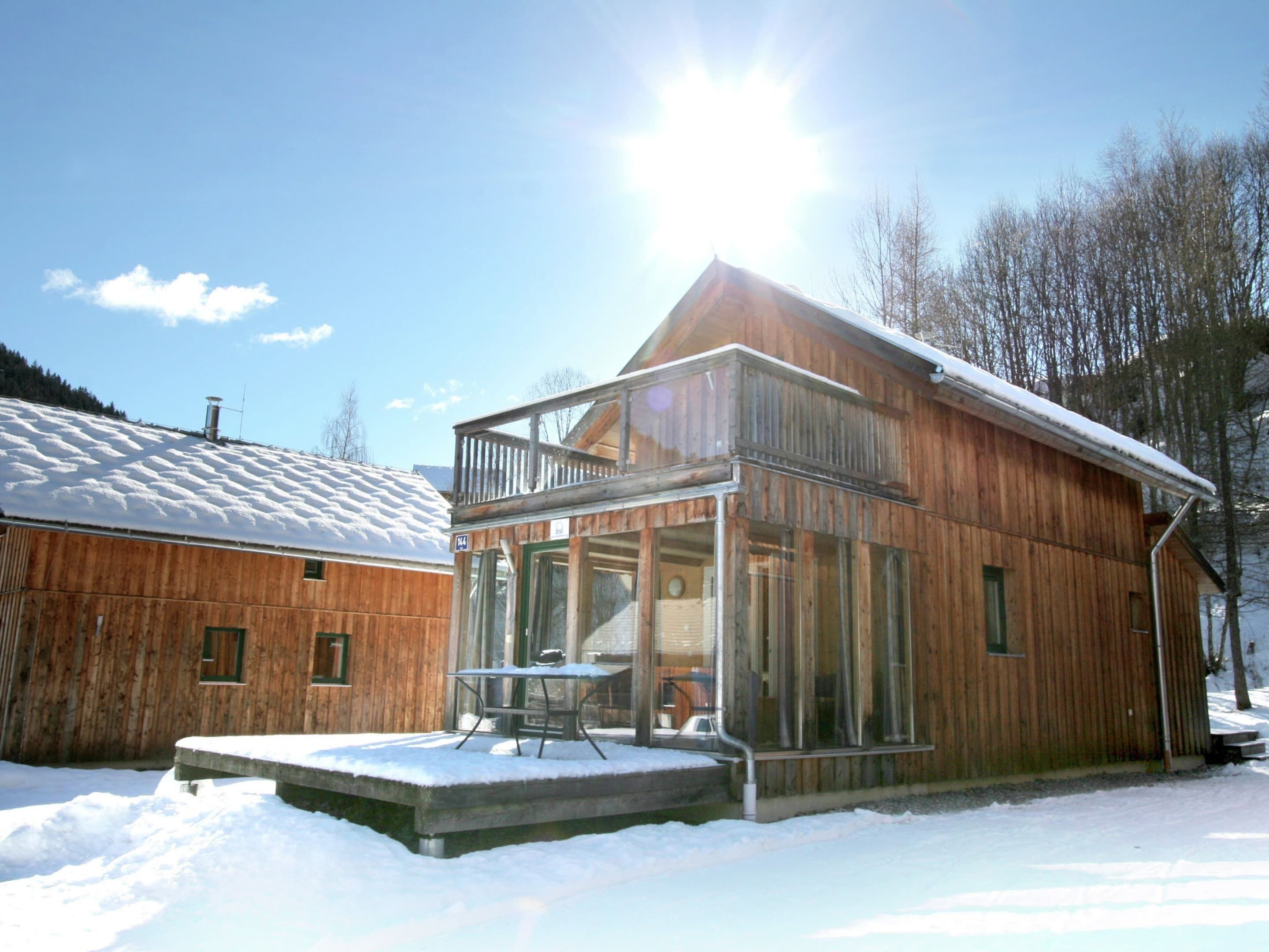 Une cabane en bois dotée d’un balcon en verre, d’un toit recouvert de neige et surplombant un ciel dégagé.