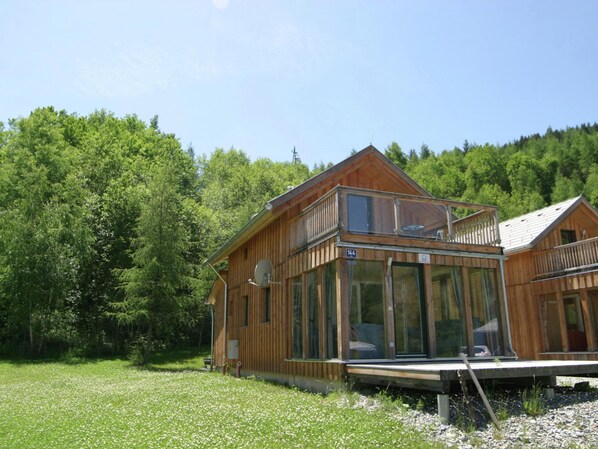 A wooden cabin with a balcony, large windows, and a number '144' sign.