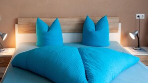 A neatly made bed with blue bedding and matching pillows, two bedside lamps, and a wooden headboard.
