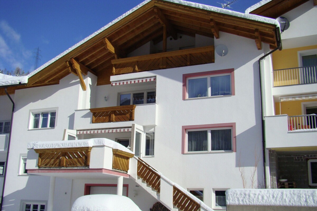 Um edifício de vários andares com varandas, vigas de madeira e um carro coberto de neve.