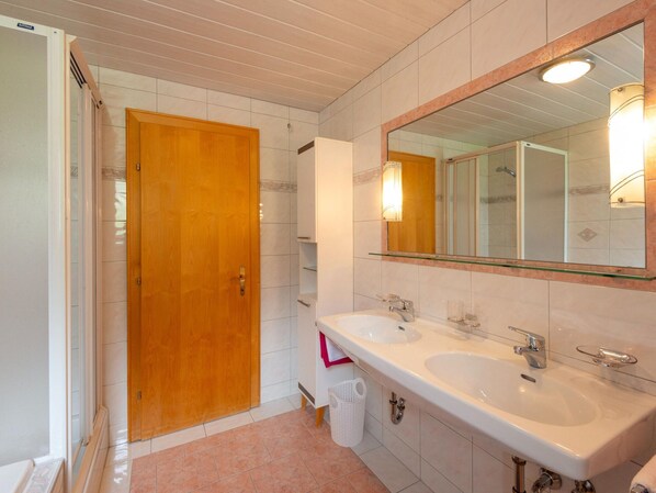 Une salle de bain avec deux lavabos, une porte en bois, un miroir et une poubelle.