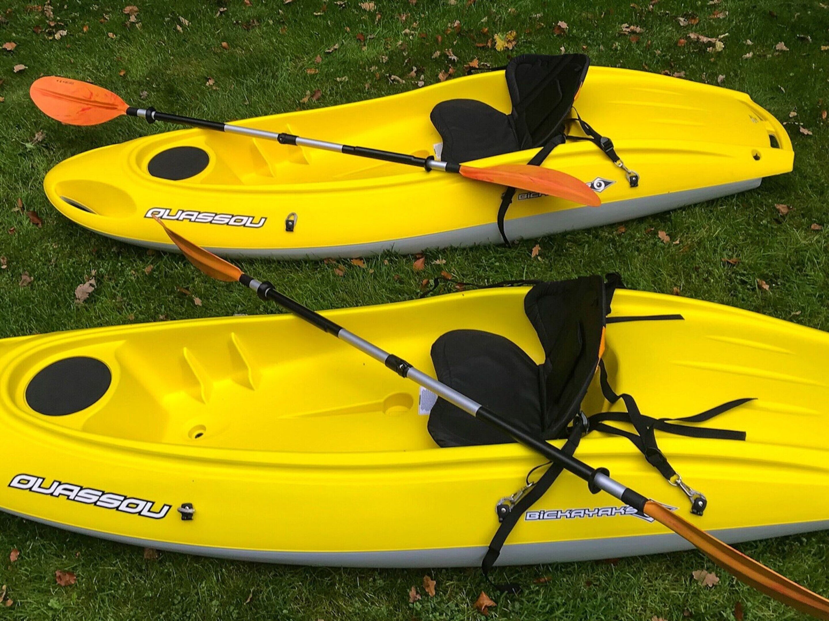 Dos kayaks amarillos con remos y chalecos salvavidas sobre césped.